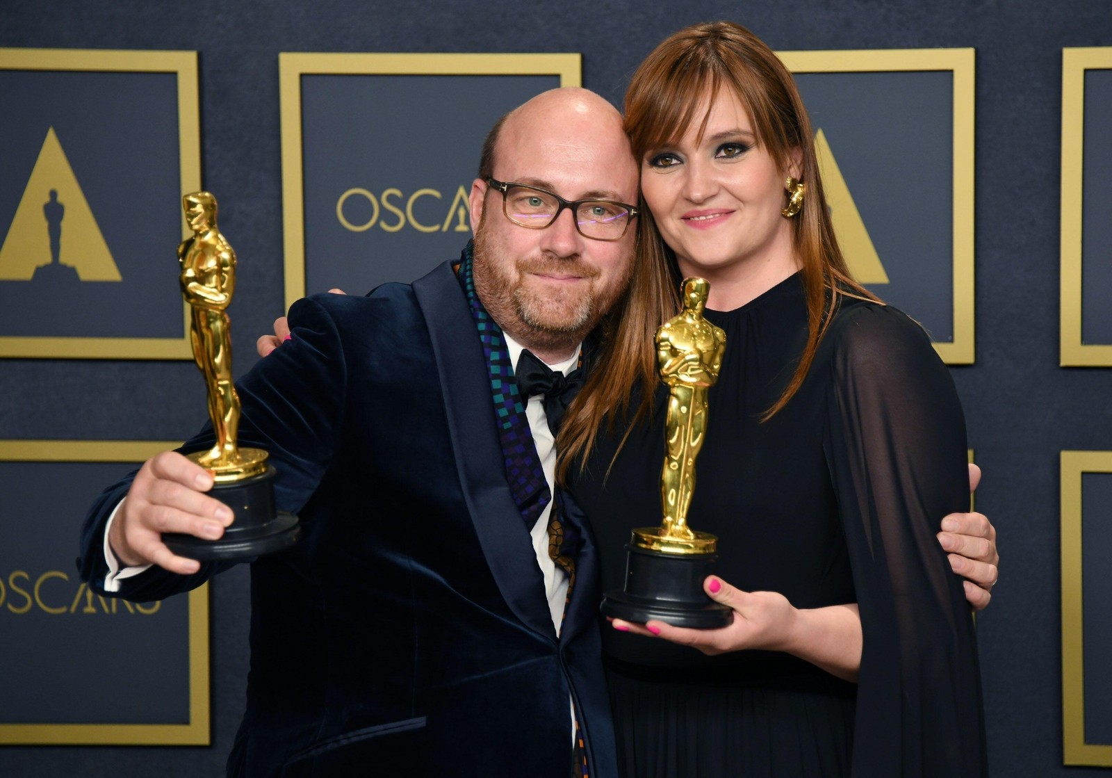  A black and white photo captures two jubilant individuals holding awards, with the gleaming statue in the foreground emphasized by the person's outstretched arm.