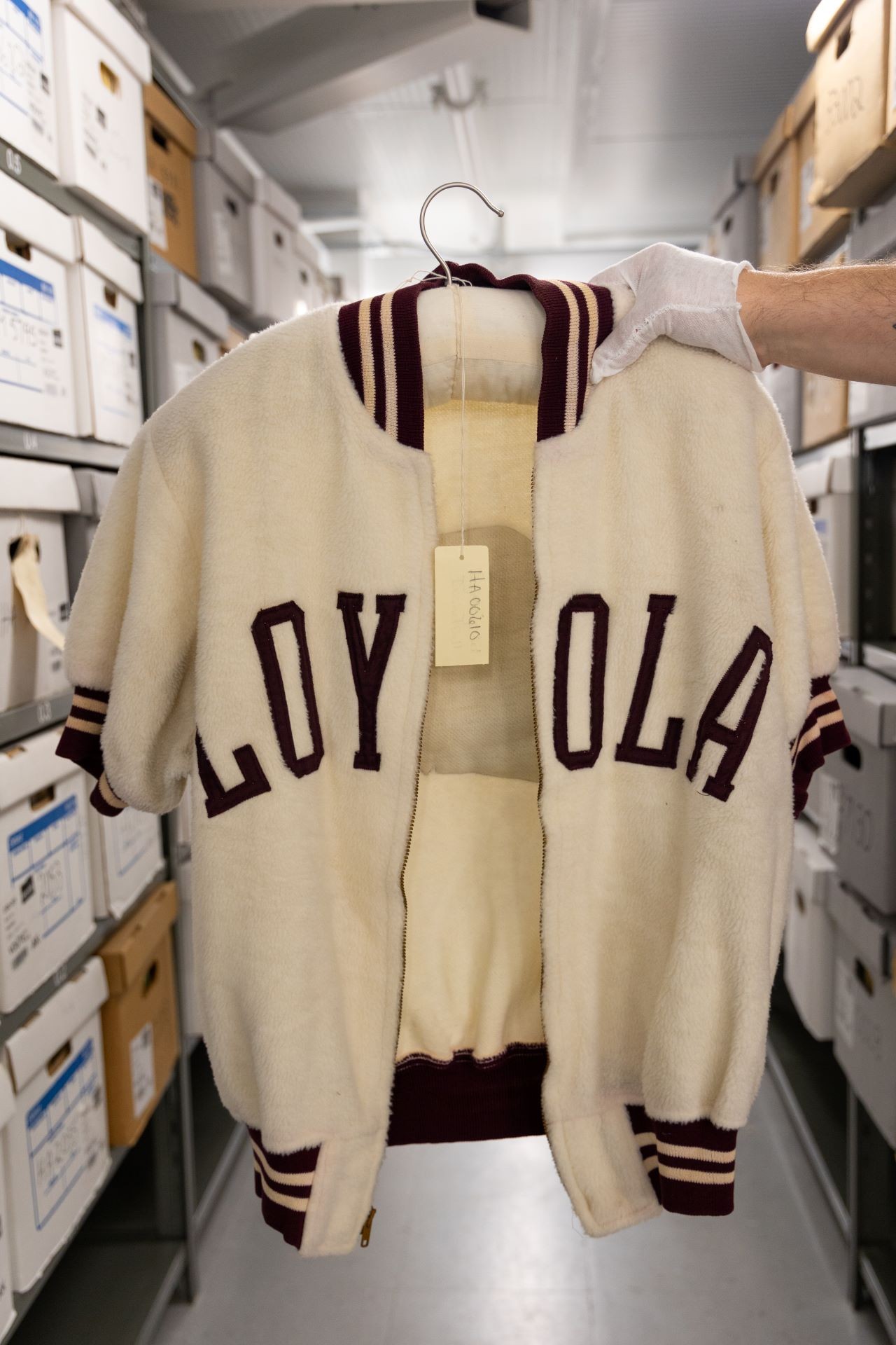 Une main tient une veste universitaire classique avec le texte « LOYOLA », symbolisant l'héritage et l'histoire sportive du collège Loyola.