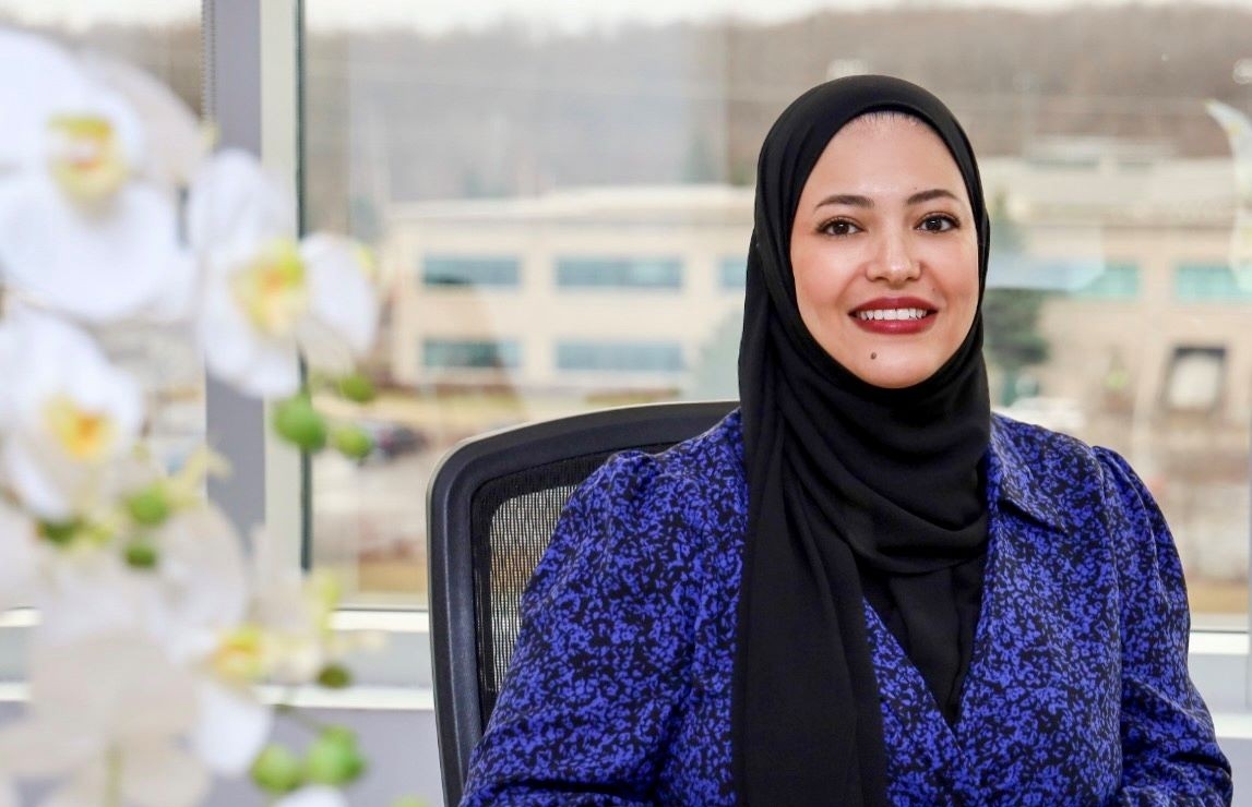 Une femme dans un cadre professionnel, assise à un bureau avec un ordinateur portable, souriant avec confiance.