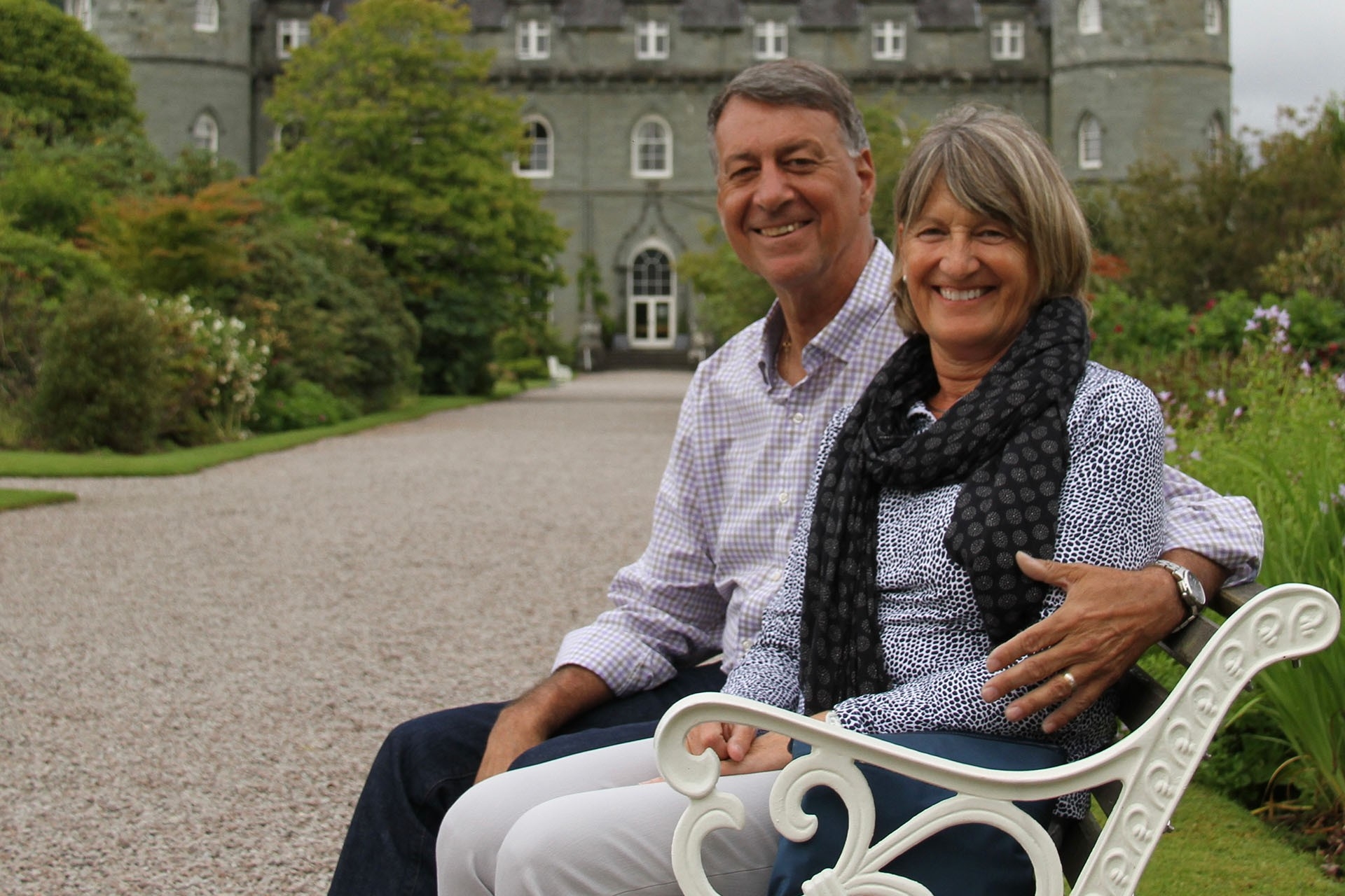 Constantine Constandis et Anne Upton-Constandis sont assis sur un banc en fer blanc sur un chemin devant un château écossais.