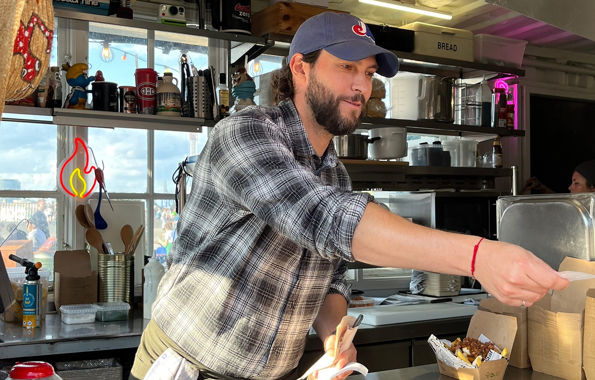Daniel porte une casquette des Expos de Montréal et une chemise en flanelle alors qu'il tend de la nourriture à un client.