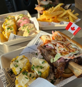 Trois portions d'épis de maïs, de bœuf, de tacos et de frites sont présentées. L'une des portions contient un petit drapeau canadien en papier.