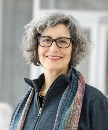 alt="une femme aux cheveux courts et aux lunettes regarde la caméra."