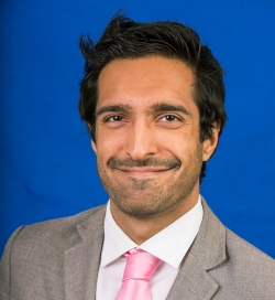 Salim Valji est un journaliste sportif qui pose devant un fond bleu. Il a les cheveux noirs et porte un blazer sur une cravate et une chemise à col.