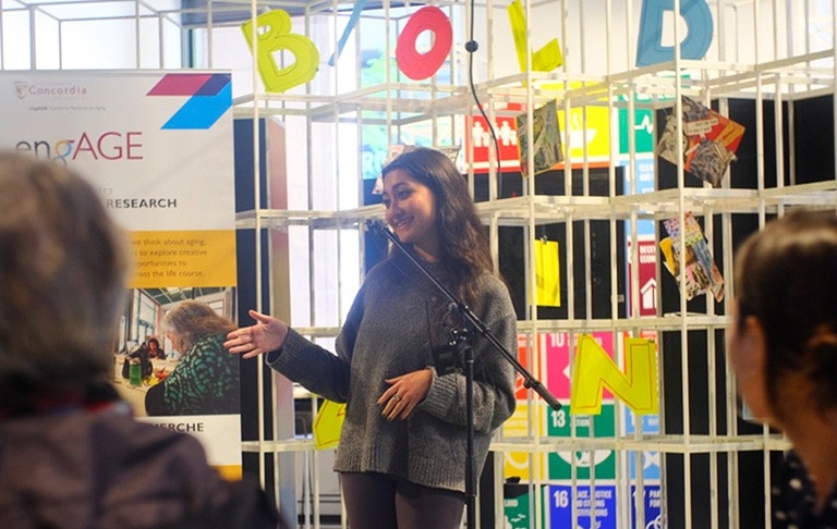 Emma se tient devant un affichage aux couleurs vives alors qu'elle s'adresse à un auditoire au 4e Espace de Concordia.