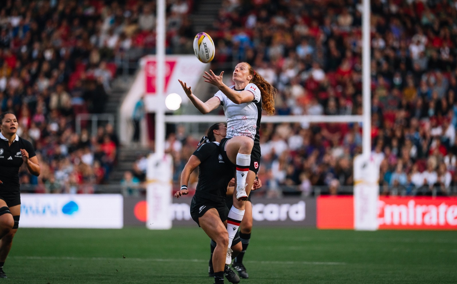 Alex Tessier Une joueuse de rugby aux longs cheveux roux, représentant l'équipe canadienne, saute en l'air pour attraper le ballon