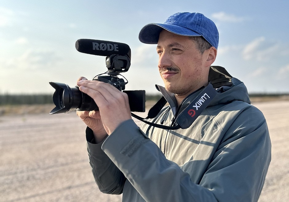 Gabriel est dehors, vêtu d'une veste et d'une casquette de baseball, tenant une caméra.