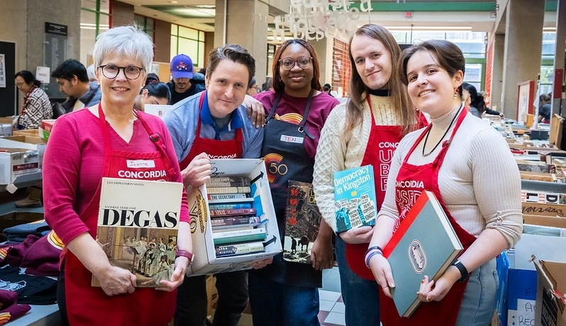 Un groupe de bénévoles, vêtus de tabliers rouges, tiennent des livres dans un grand atrium rempli de rangées de livres.