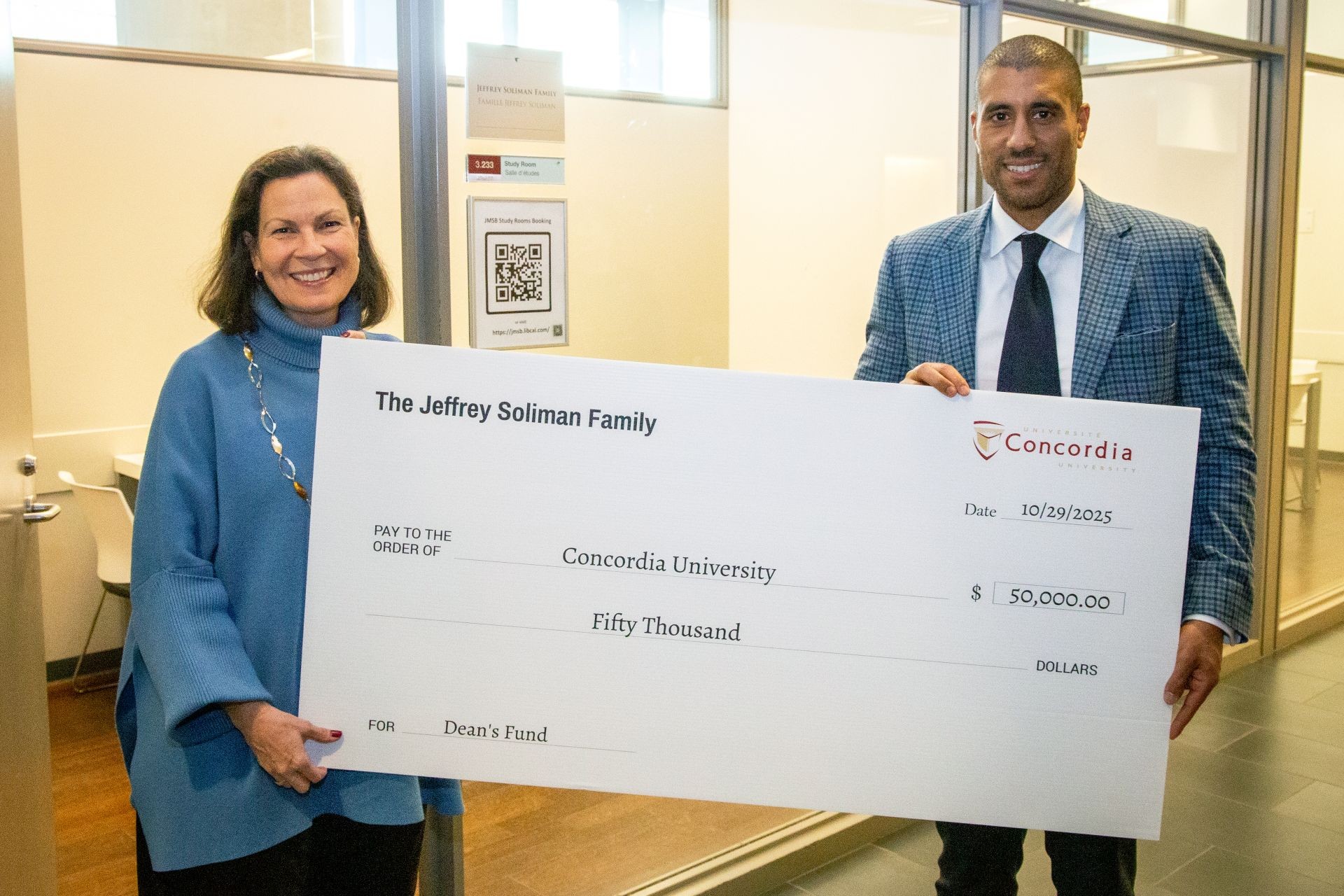 Une femme aux cheveux foncés vêtue d'un chandail bleu et un homme portant une veste à carreaux tiennent un chèque géant d'un montant de 50 000 $ à l'ordre de Concordia, offert par la famille Soliman.