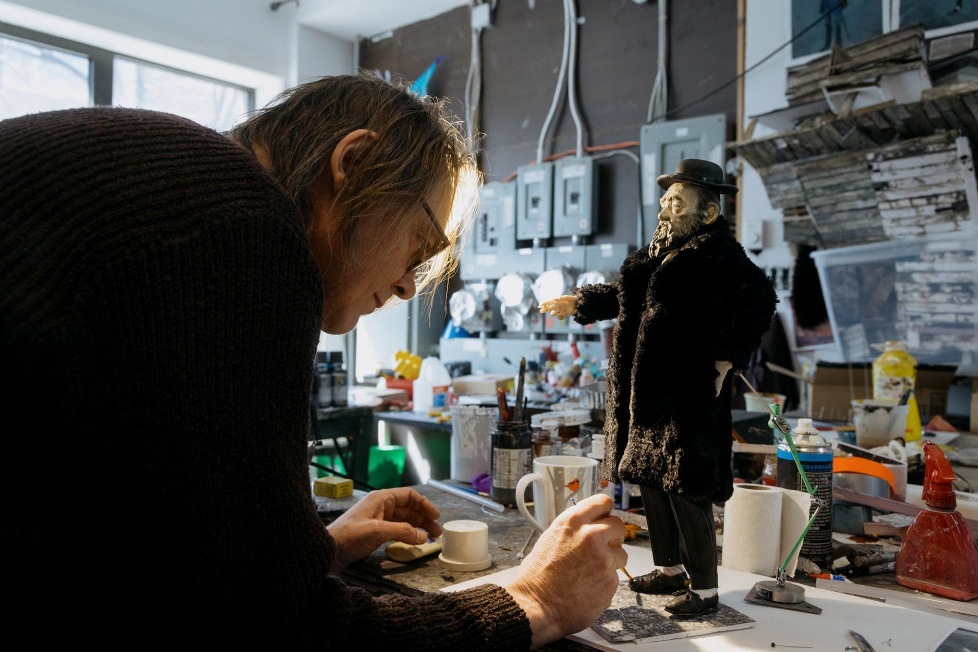 Un homme assis à un établi dans un atelier d'art se penche sur un chiot tout en peignant des détails sur ses pattes. 