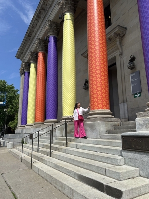 Skawennati se tient devant un bâtiment dont les colonnes sont recouvertes de ses œuvres colorées.