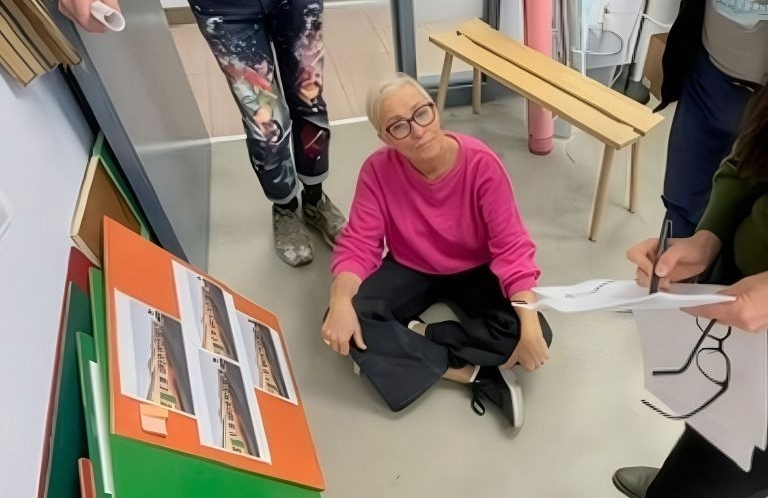 Élise est assise par terre, entourée des membres de son équipe qui examinent des échantillons de couleurs et des storyboards.