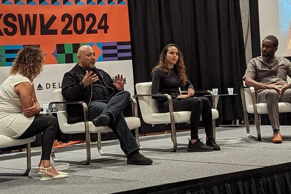 Quatre personnes assises sur des chaises sur une scène surélevée, deux hommes et deux femmes, avec une bannière en arrière-plan avec le texte suivant "SXSW 2024".