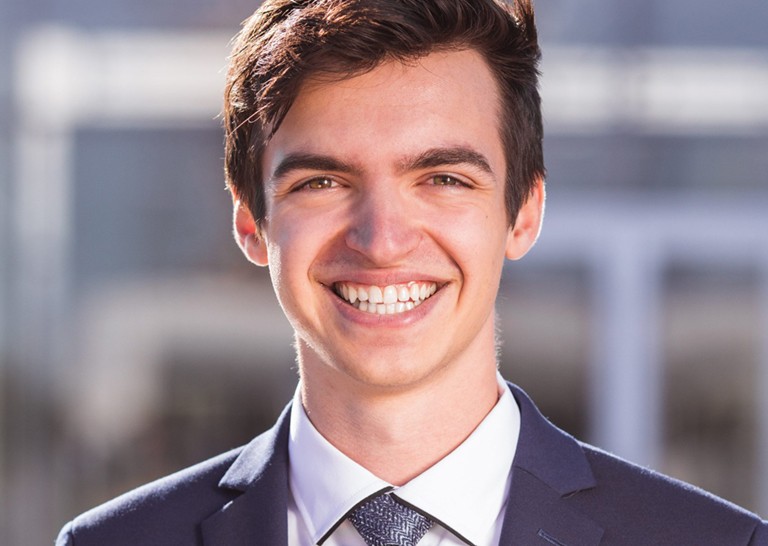 Un jeune homme souriant avec de courts cheveux noirs et un costume bleu et une cravate.