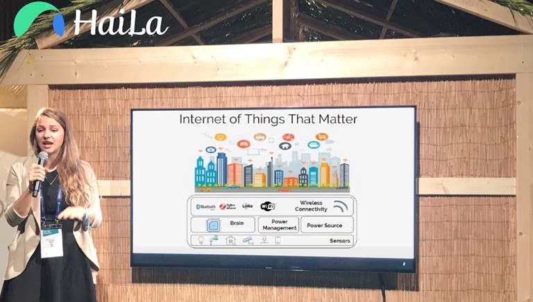 Young, blonde woman giving a presentation with a microphone and a board in the background that says, 'Internet of things that matter."