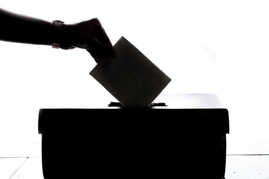 Silhouette d'une main qui insère un bulletin de vote dans une boite de scrutin 