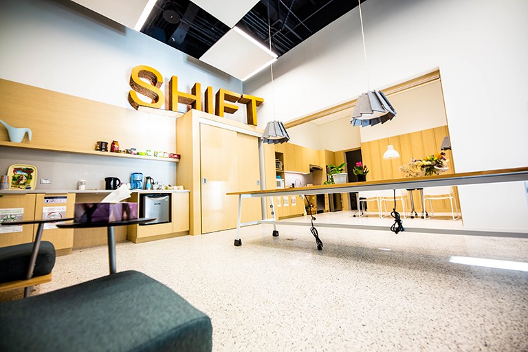 An open space with desks and chairs and a big sign on the wall that says, SHIFT