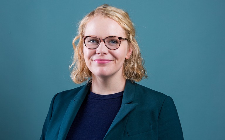 Jeune femme souriante à lunettes, cheveux blonds mi-longs, portant un blazer sarcelle et un haut bleu