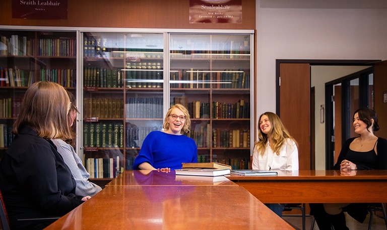 A group of laughing young people sitting round desks in a library settting