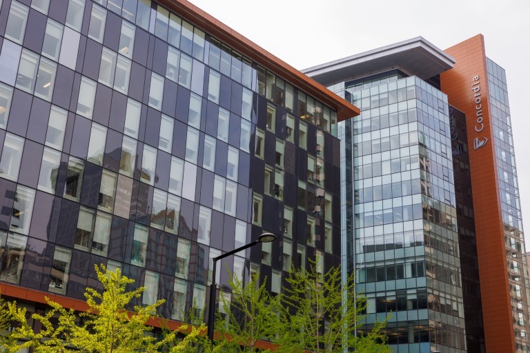 Mise à jour sur le budget de 2024-2025 Un bâtiment moderne en verre avec l'inscription « Concordia » sur un côté. Le bâtiment présente un mélange de fenêtres sombres et transparentes, et des arbres au premier plan.