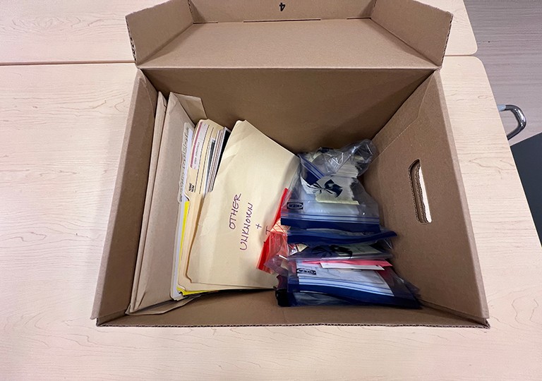 Une boîte de documents provenant du Service des loisirs et des sports, avant un traitement de 24 heures. Une boîte de photos posée sur une table