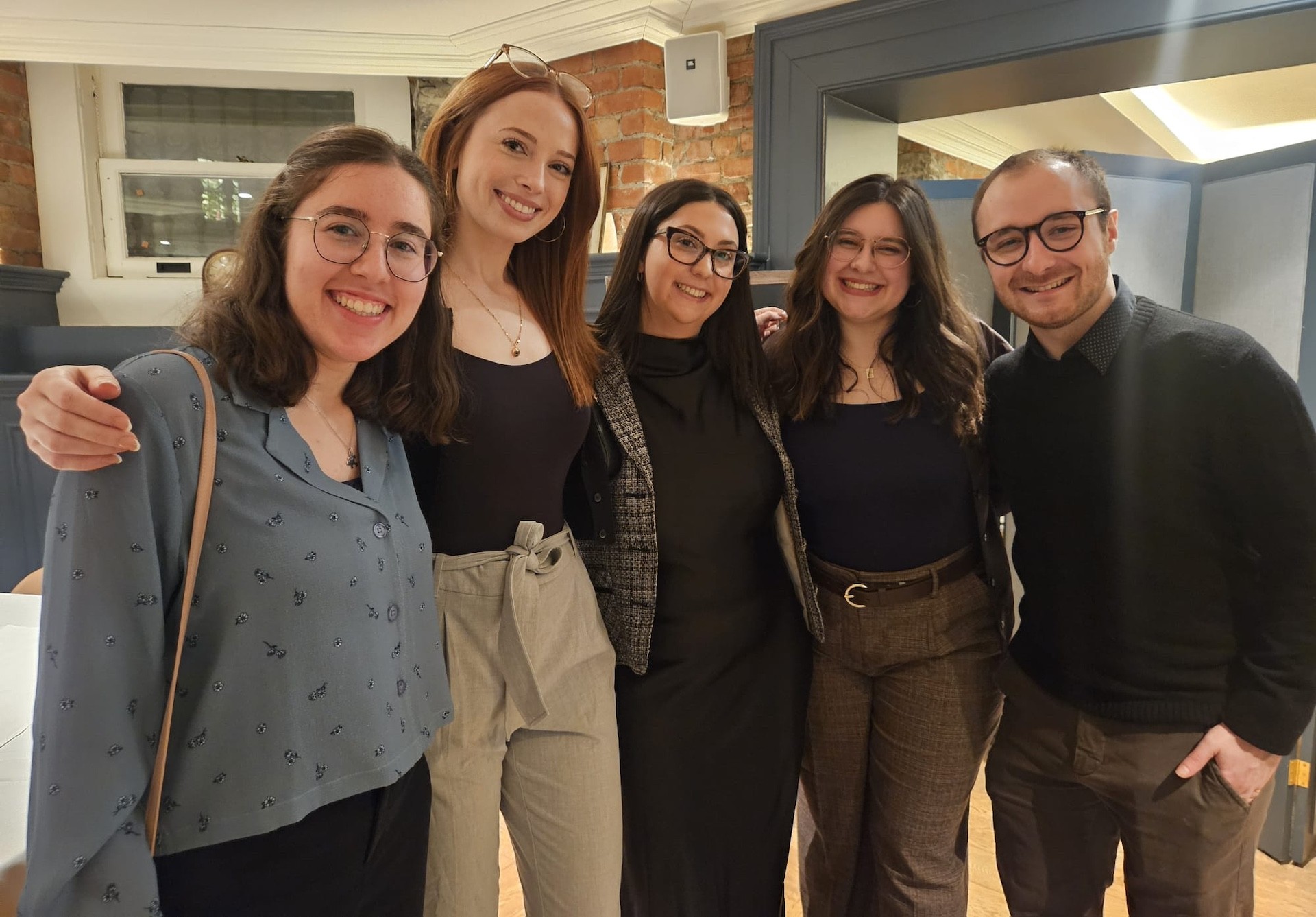 Un groupe souriant de quatre femmes et un homme, bras dessus bras dessous