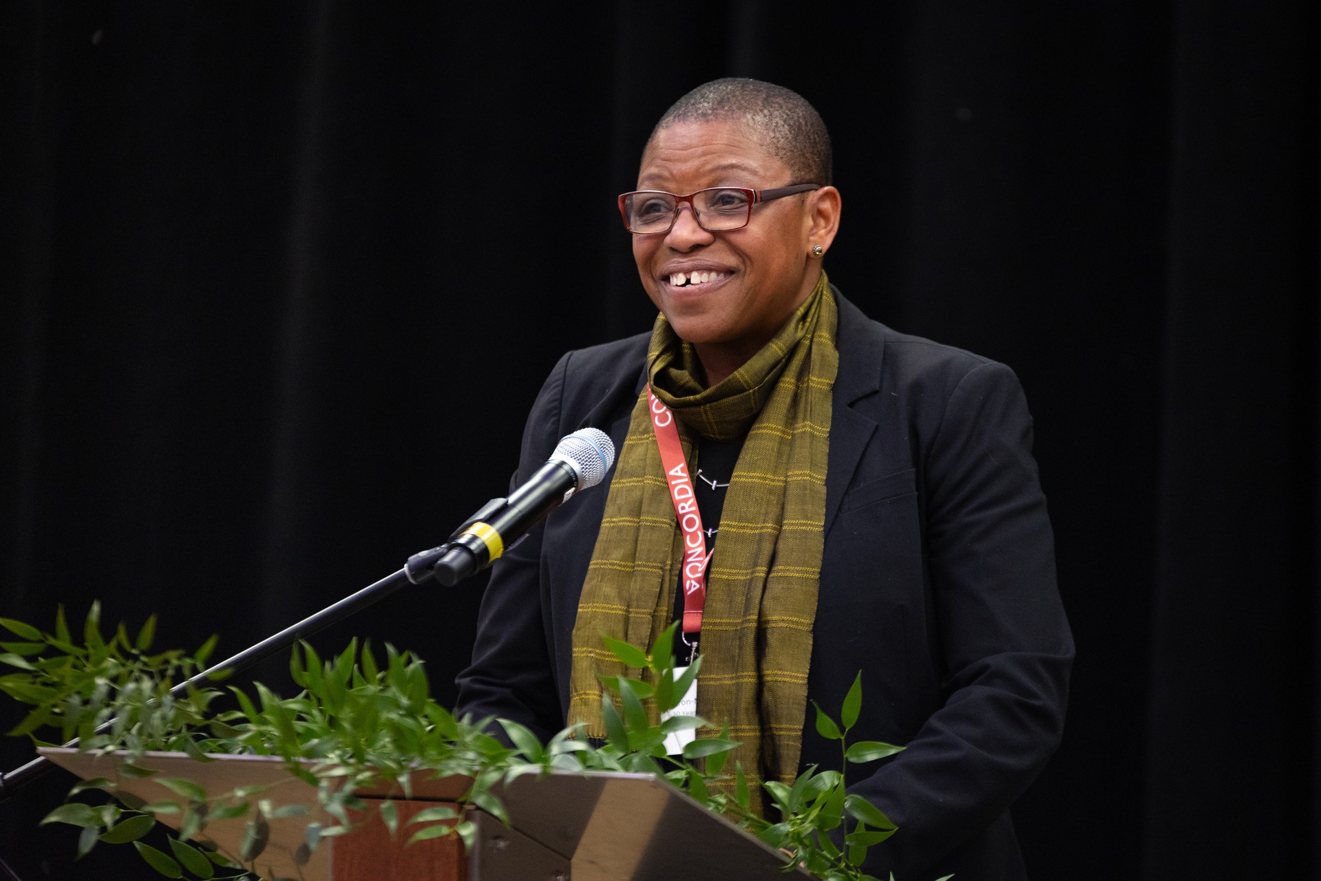 A black woman wearing glasses, standing at a lectern.