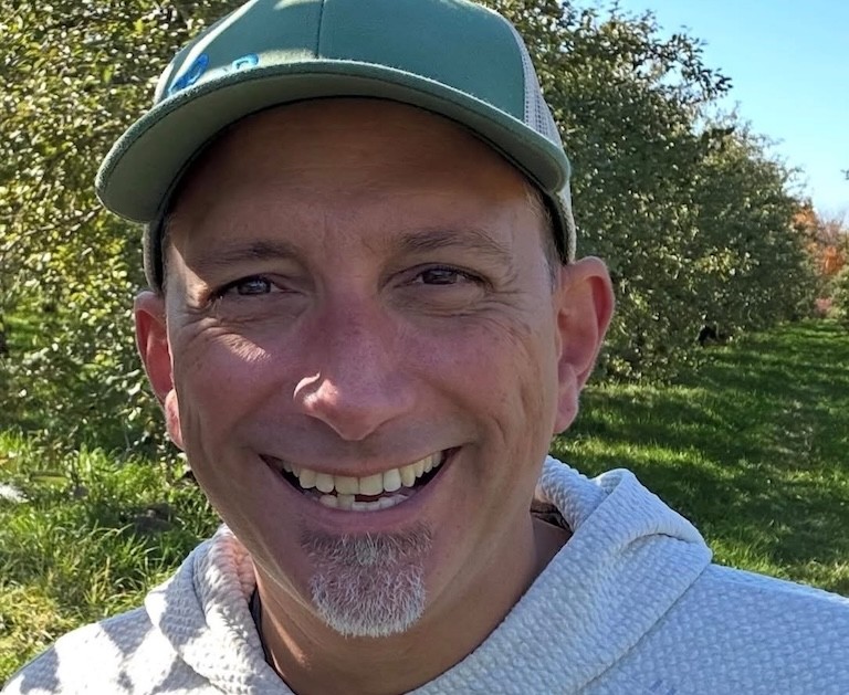 Close-up of a smilling middle-aged man wearing a ball cap outside in shade